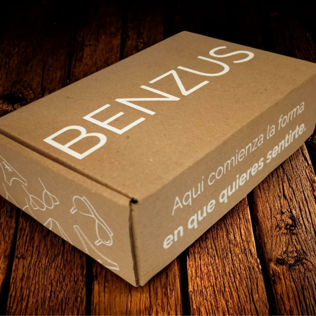 Primer plano de la caja de envío de cartón microcorrugado de BENZUS. Muestra el logo 'BENZUS' en blanco y el mensaje frontal 'Aquí comienza la forma en que quieres sentirte'. El diseño incluye ilustraciones de ropa interior de manera sutil en la parte inferior y lateral de la caja.